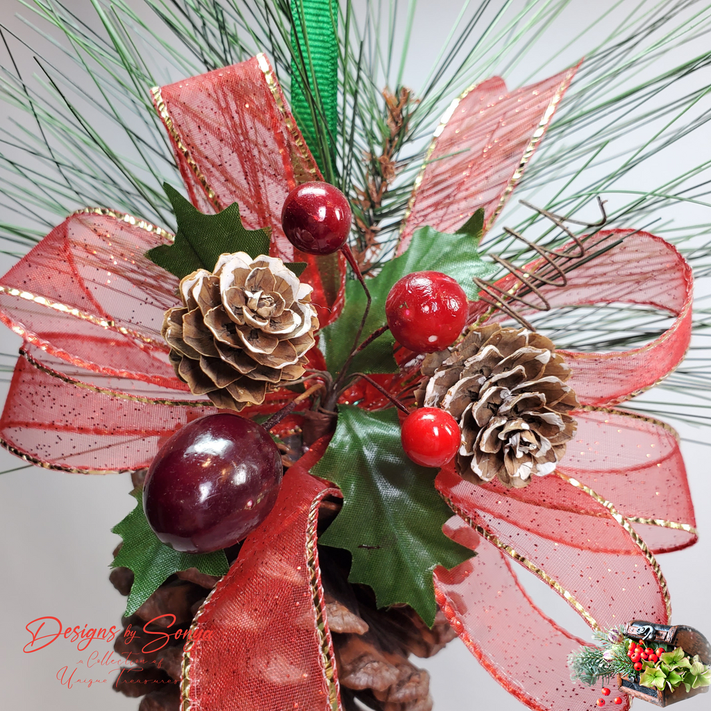 Top Close-Up with Green Sprigs
Handmade pinecone ornament showcasing red berries, holly leaves, glittered ribbon, and frosted pinecone tips with lifelike evergreen sprigs for rustic holiday style.
