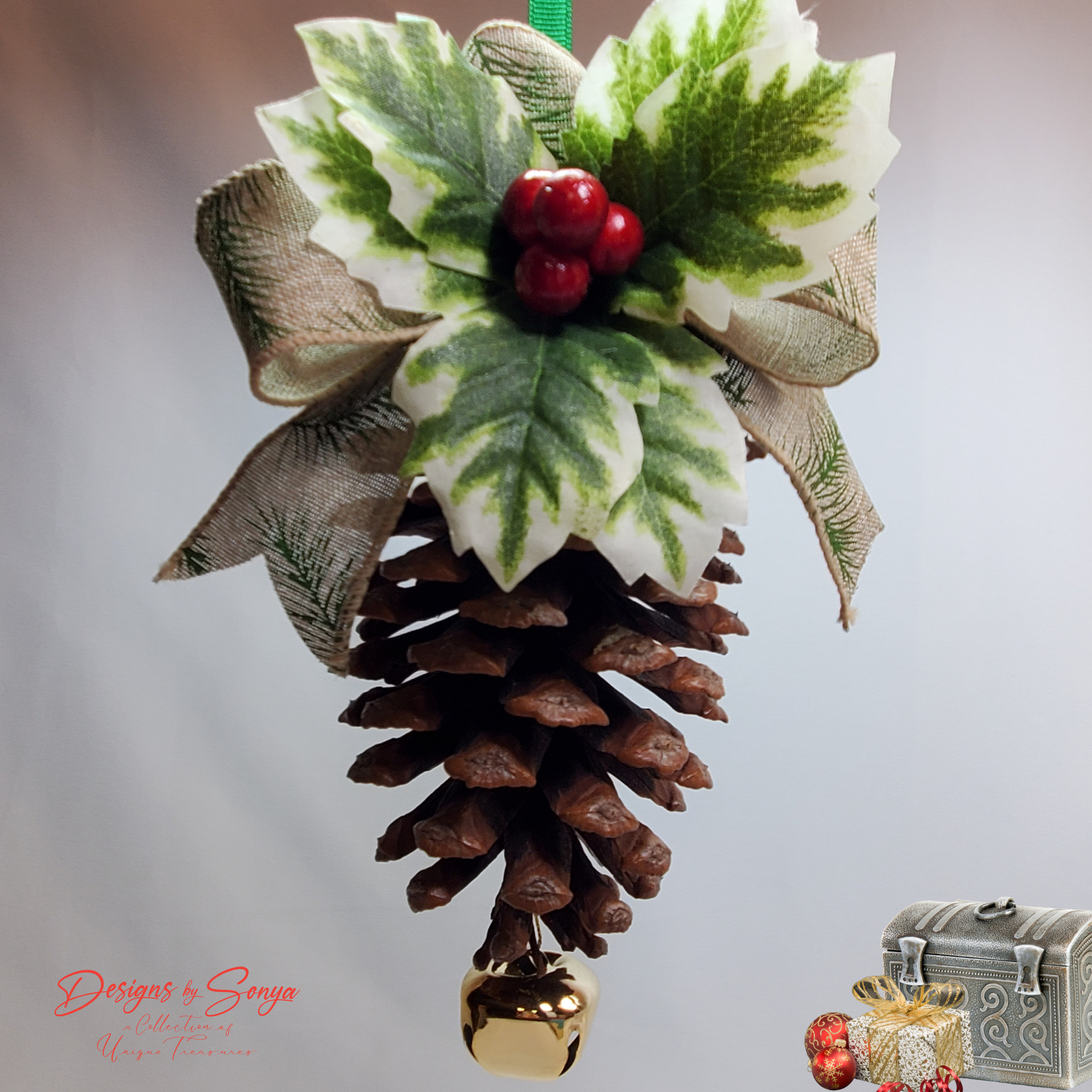 Warm-Tone Hanging Close View
Rustic handmade pinecone ornament shown hanging, highlighting layered holly leaves, red berry cluster, burlap ribbon loops and polished gold bell; cozy holiday accent.