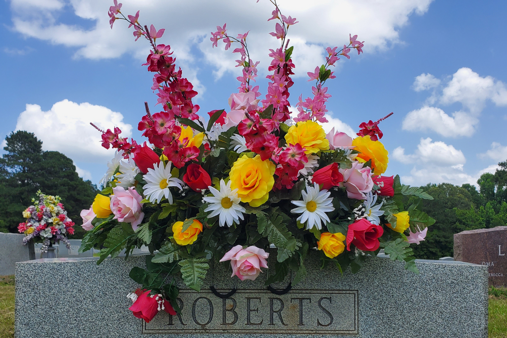 Bright Headstone Saddle with Mixed Florals
Artificial spring and summer headstone saddle featuring yellow roses, pink roses, white daisies, and red tulips with greenery on a granite memorial.