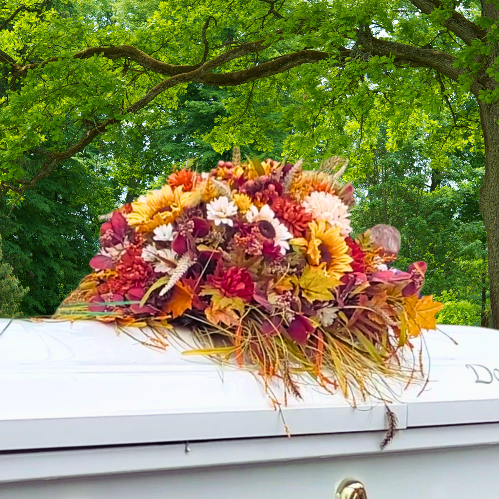 Fall Headstone Saddle on Gravestone
Artificial fall headstone saddle with sunflowers, red mums, white daisies, pinecones, and wheat accents displayed on a gray stone memorial.